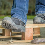 A person with blue jeans and black shoes standing on top of wooden platform.
